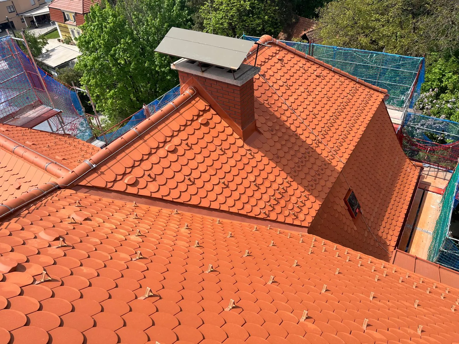 Rote Rundschnittdeckung mit Gaube und Kamin an einer gegliederten Dachfläche