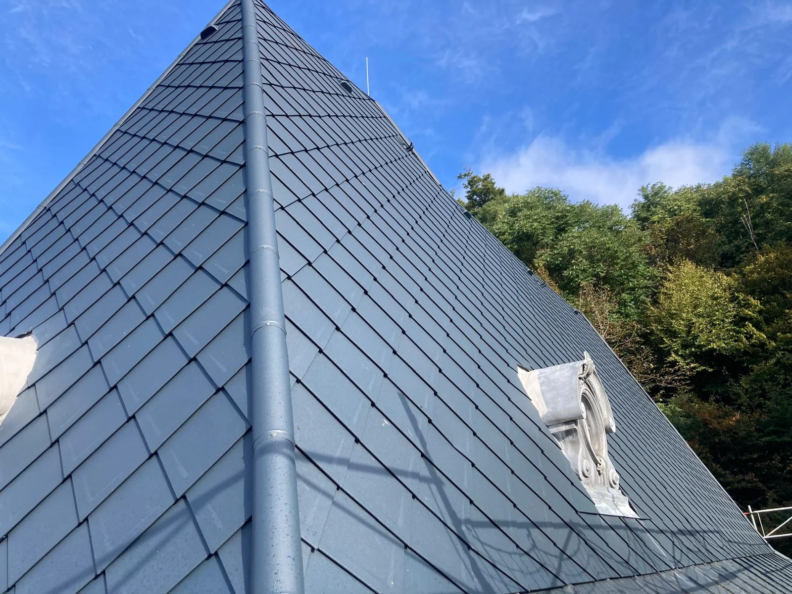 Steiles graues Rautendach mit Dachgrat und ornamentierter Rundfenstereinfassung