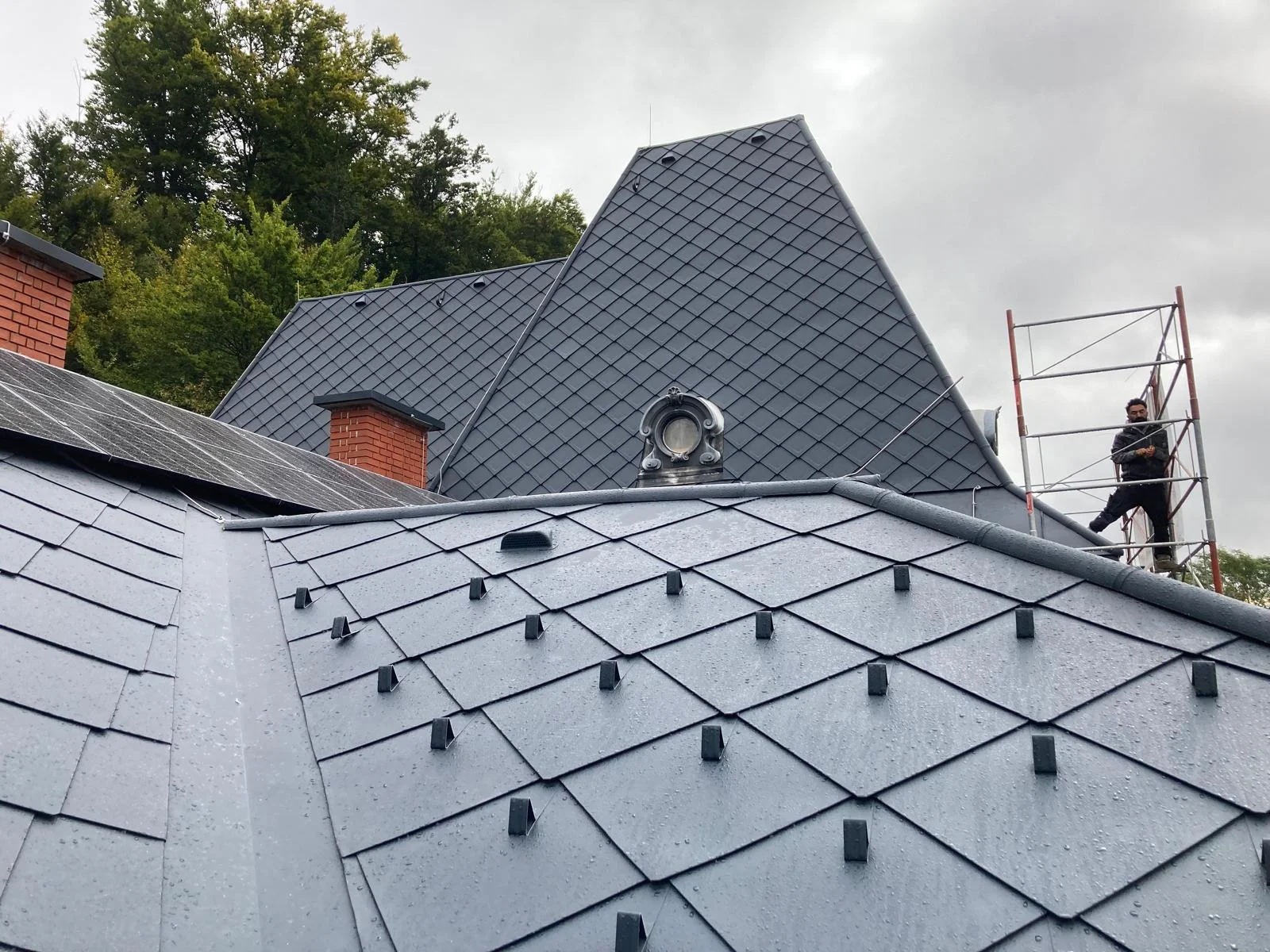 Mehrere graue Dachflächen mit Rautendeckung, Schneefangelementen und Rundfenster