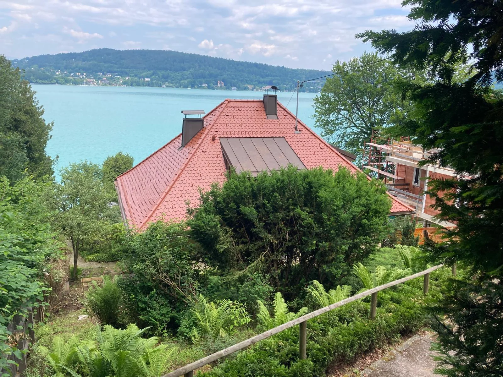 Seitliche Ansicht der roten Dachflächen und der Gaube mit dem Wörthersee im Hintergrund